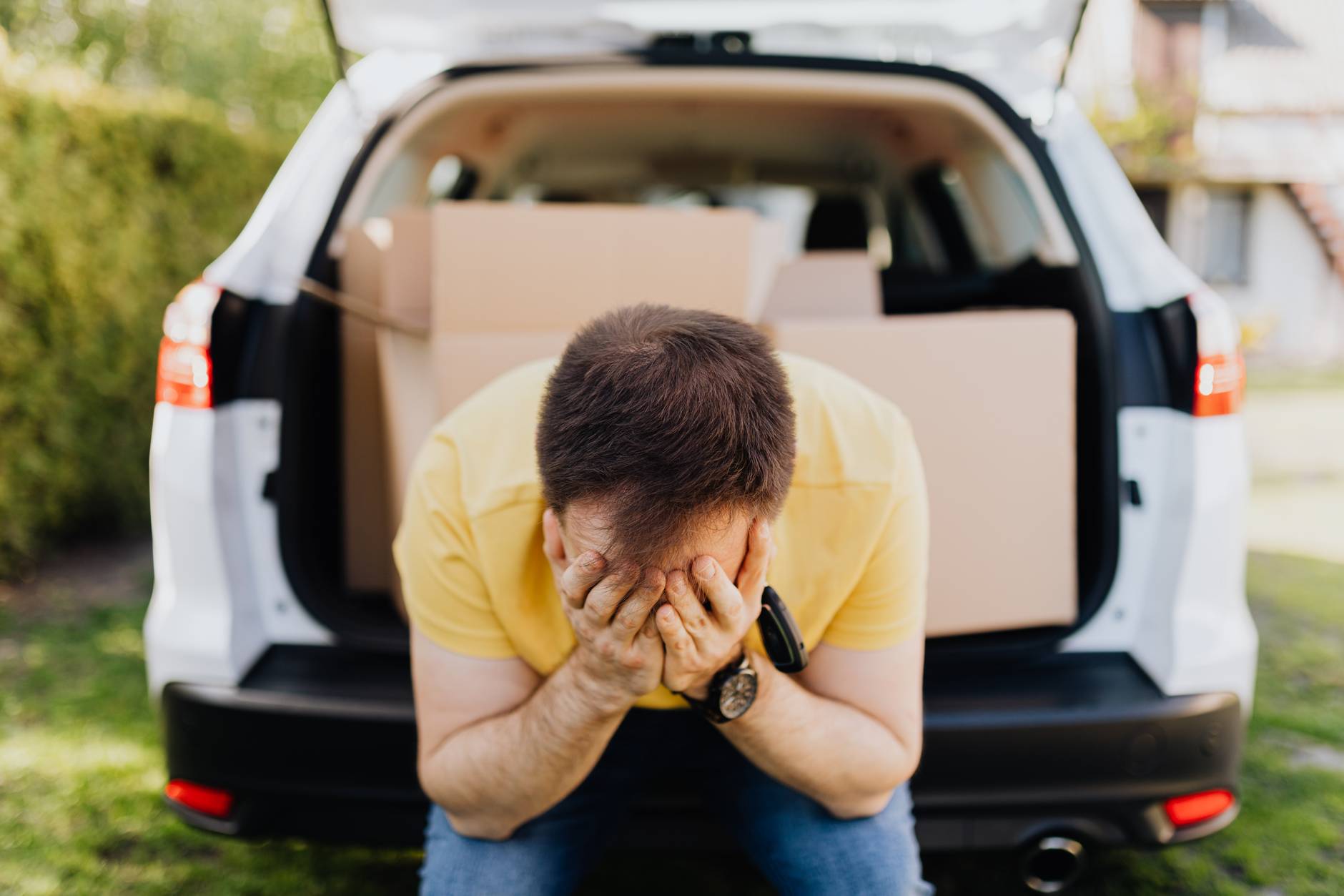 man covering face with hands near car trunk